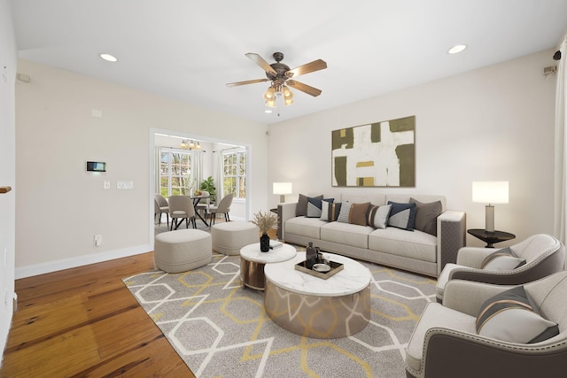 living area with ceiling fan with notable chandelier, recessed lighting, wood finished floors, and baseboards