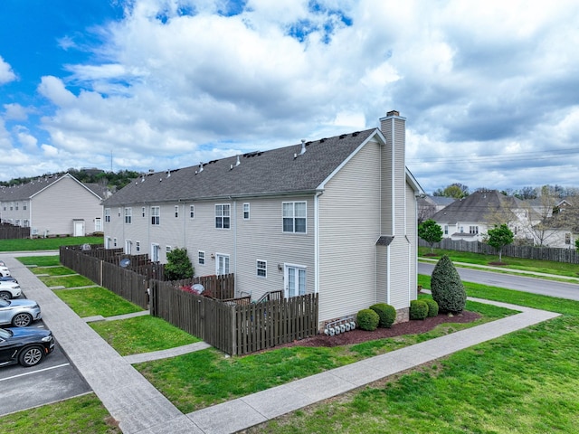 view of side of home featuring a residential view, uncovered parking, a chimney, a yard, and fence