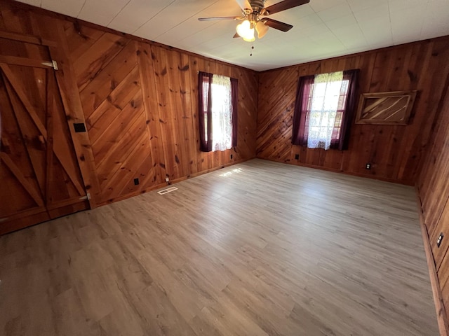 empty room featuring wood walls, a ceiling fan, light wood-style floors, and visible vents