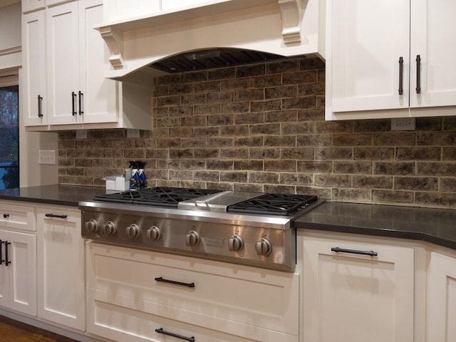 kitchen featuring white cabinetry, tasteful backsplash, stainless steel gas cooktop, dark countertops, and wall chimney range hood