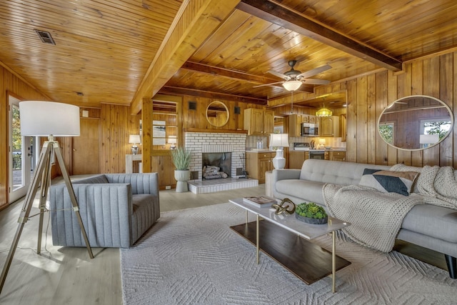 living room featuring light wood finished floors, beamed ceiling, wood walls, and a ceiling fan