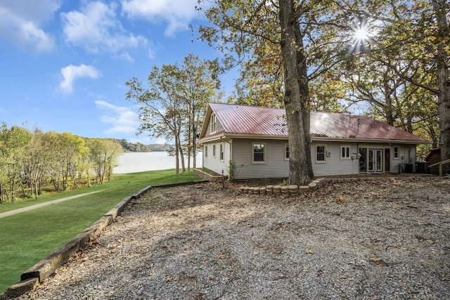rear view of property featuring french doors, a water view, a yard, and metal roof