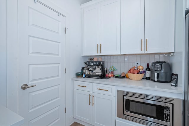 kitchen with tasteful backsplash, light countertops, white cabinets, and stainless steel microwave