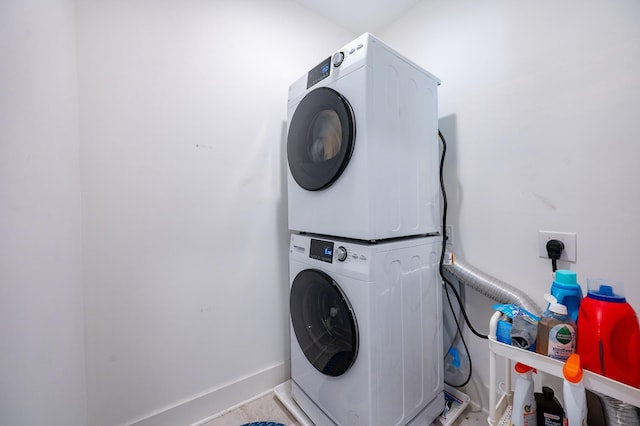 clothes washing area with baseboards, stacked washing maching and dryer, and laundry area