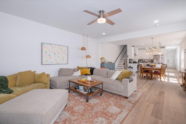 living area featuring light wood-style floors, recessed lighting, stairway, and ceiling fan with notable chandelier
