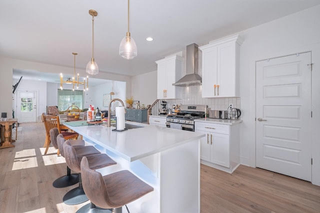 kitchen featuring wall chimney range hood, a sink, gas range, and light wood-type flooring