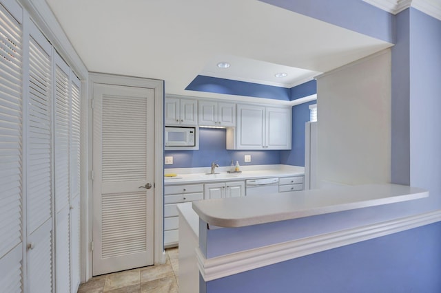 kitchen featuring light countertops, white appliances, a raised ceiling, a sink, and a peninsula