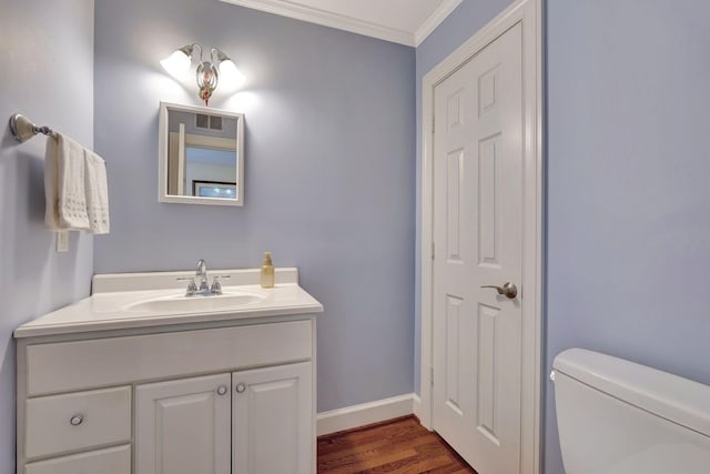 bathroom with vanity, crown molding, toilet, baseboards, and wood finished floors