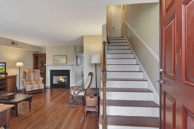stairway with a warm lit fireplace, visible vents, and wood finished floors