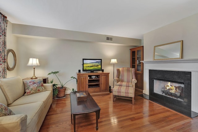 living room featuring a lit fireplace, visible vents, and hardwood / wood-style floors
