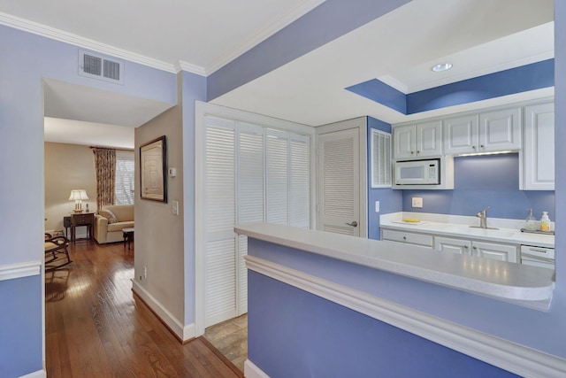 kitchen with light countertops, crown molding, visible vents, light wood-style flooring, and white microwave