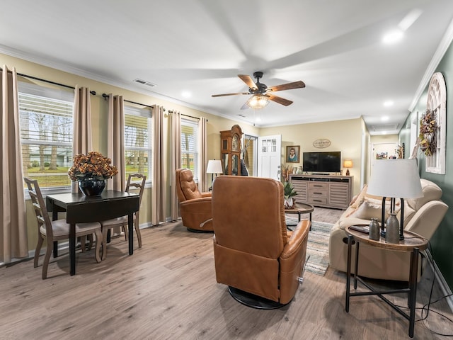 living area with ornamental molding, visible vents, light wood-style floors, and a ceiling fan