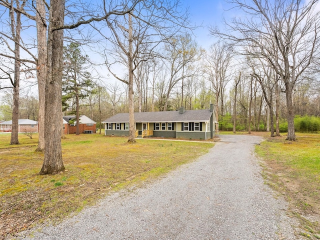 view of front of house featuring gravel driveway, a front lawn, and a chimney