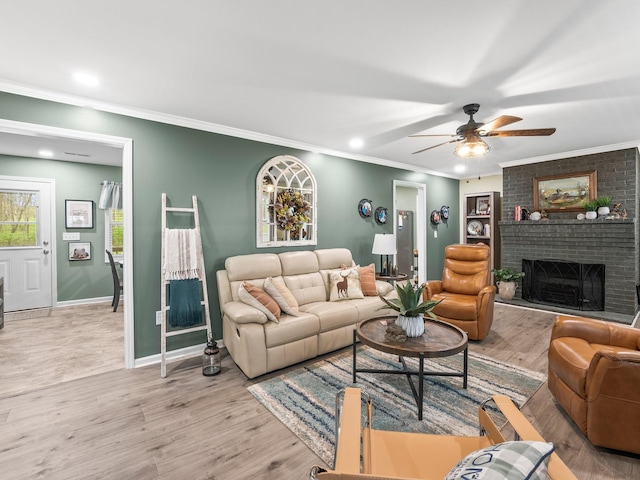 living area featuring a brick fireplace, ornamental molding, baseboards, a ceiling fan, and wood finished floors