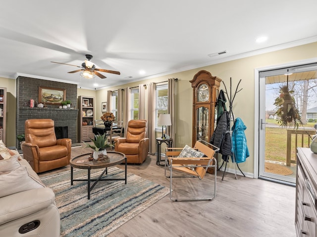living area featuring light wood-style flooring, visible vents, a fireplace, ornamental molding, and a ceiling fan