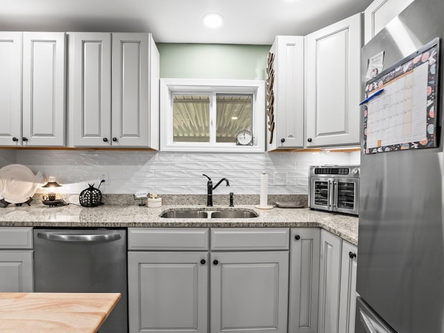 kitchen with white cabinetry, decorative backsplash, a sink, light stone counters, and appliances with stainless steel finishes
