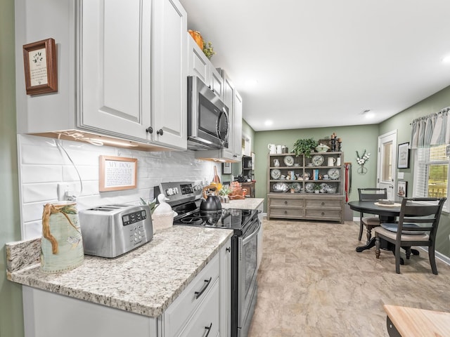 kitchen with white cabinetry, backsplash, light stone countertops, and appliances with stainless steel finishes
