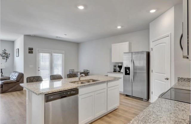 kitchen featuring an island with sink, light wood-style flooring, appliances with stainless steel finishes, a sink, and white cabinetry