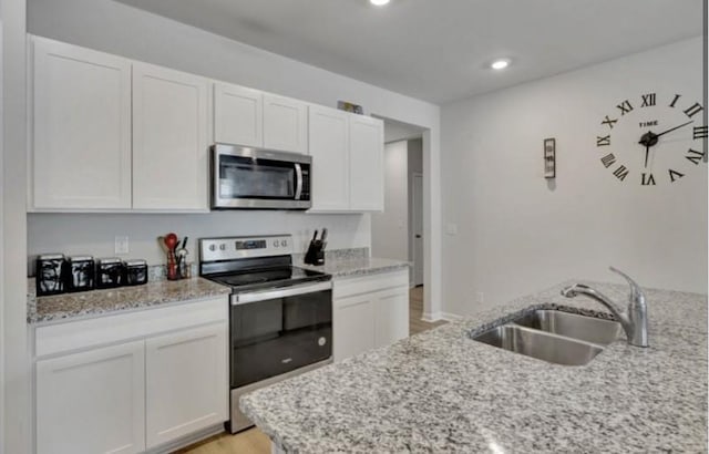 kitchen featuring recessed lighting, light stone counters, stainless steel appliances, a sink, and white cabinetry