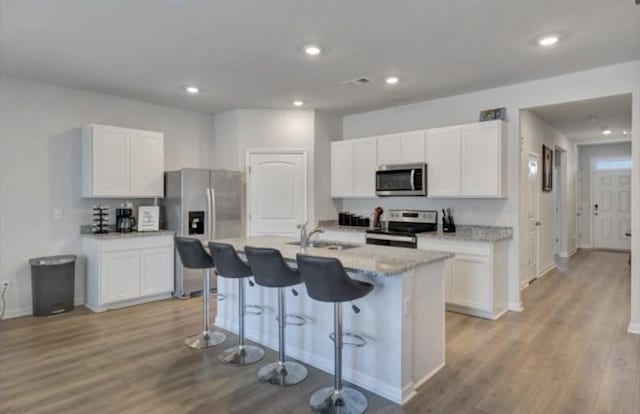 kitchen with a sink, light wood-style floors, a kitchen breakfast bar, white cabinets, and appliances with stainless steel finishes