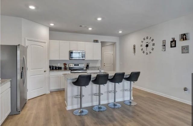 kitchen featuring white cabinetry, a breakfast bar, stainless steel appliances, baseboards, and light wood finished floors