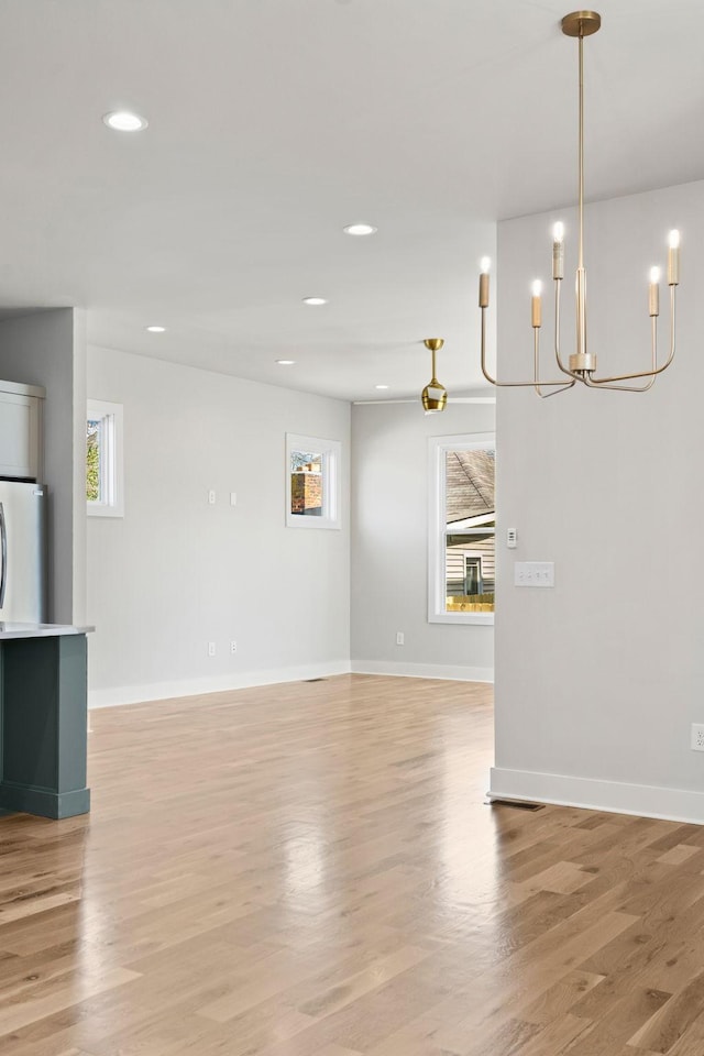 unfurnished living room featuring a wealth of natural light, light wood-style floors, baseboards, and a chandelier