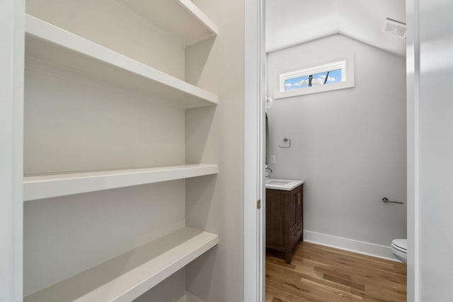 bathroom with vanity, toilet, baseboards, visible vents, and wood finished floors