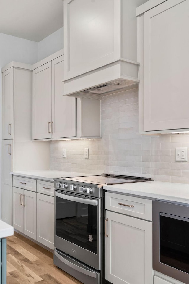 kitchen featuring light countertops, backsplash, stainless steel appliances, custom range hood, and light wood-style floors