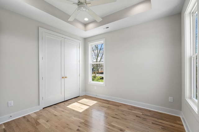 unfurnished bedroom featuring baseboards, visible vents, light wood-style flooring, and a raised ceiling