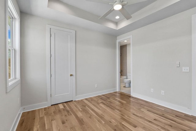unfurnished bedroom featuring connected bathroom, baseboards, light wood-style flooring, and a raised ceiling