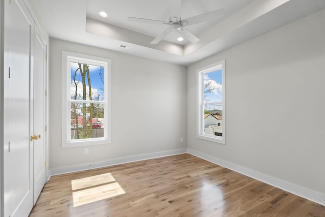 empty room featuring baseboards, a wealth of natural light, light wood finished floors, and a raised ceiling