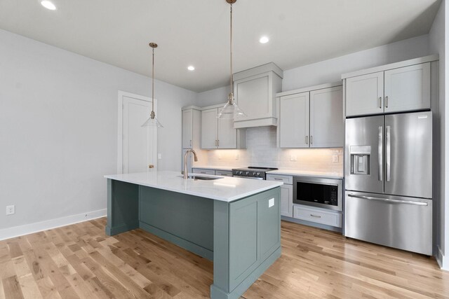 kitchen with light countertops, a sink, appliances with stainless steel finishes, light wood-style flooring, and decorative backsplash