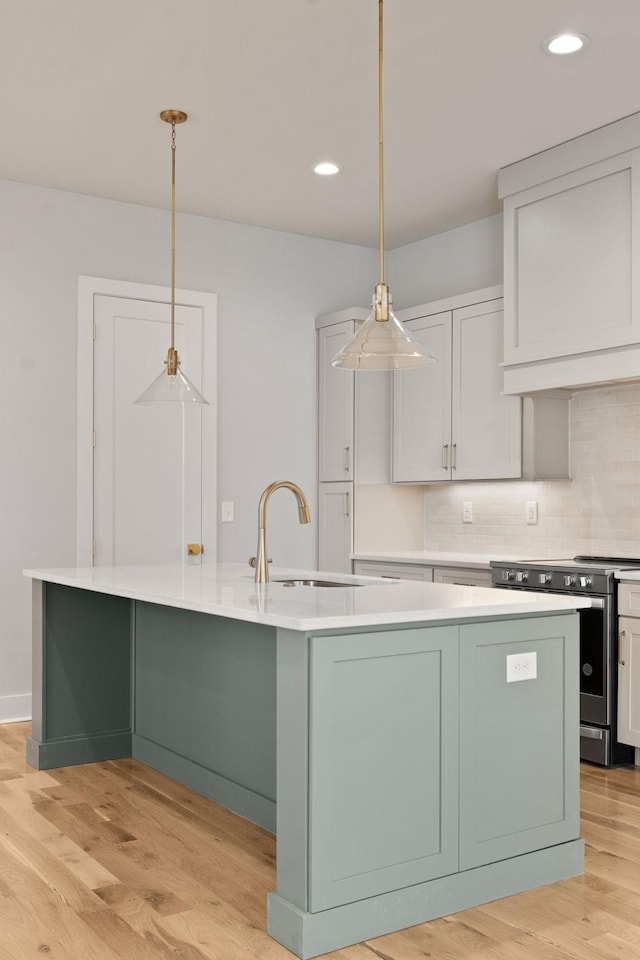 kitchen featuring a large island with sink, light countertops, a sink, tasteful backsplash, and electric stove