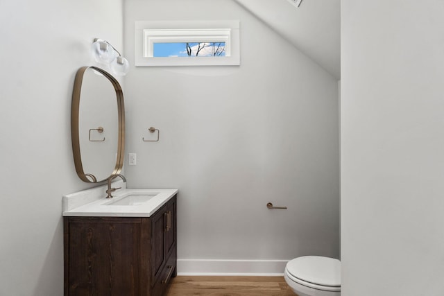 half bath featuring toilet, vanity, baseboards, and wood finished floors