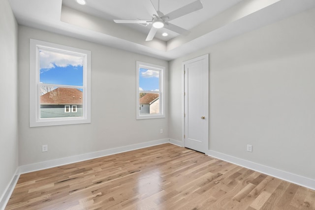 empty room with a raised ceiling, baseboards, and light wood-type flooring