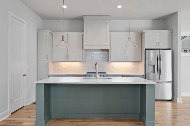 kitchen featuring stainless steel fridge with ice dispenser, light countertops, light wood-style flooring, and a center island with sink