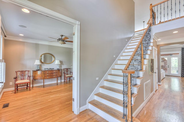 stairway featuring wood finished floors, visible vents, a ceiling fan, ornamental molding, and baseboards