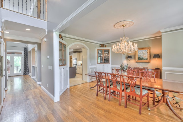 dining space with arched walkways, light wood finished floors, and ornamental molding