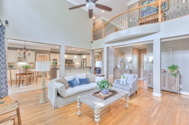 living area with a high ceiling, ornamental molding, light wood-style flooring, and ceiling fan with notable chandelier
