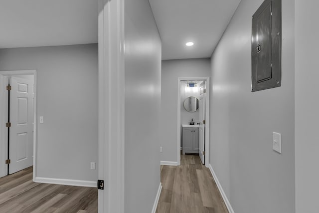 corridor featuring baseboards, light wood-style floors, and electric panel