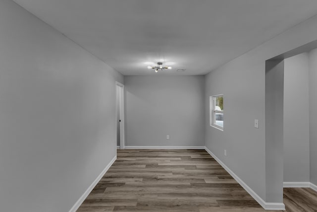 unfurnished room featuring a chandelier, baseboards, and wood finished floors