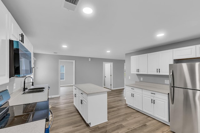 kitchen featuring appliances with stainless steel finishes, light wood finished floors, a sink, and a kitchen island