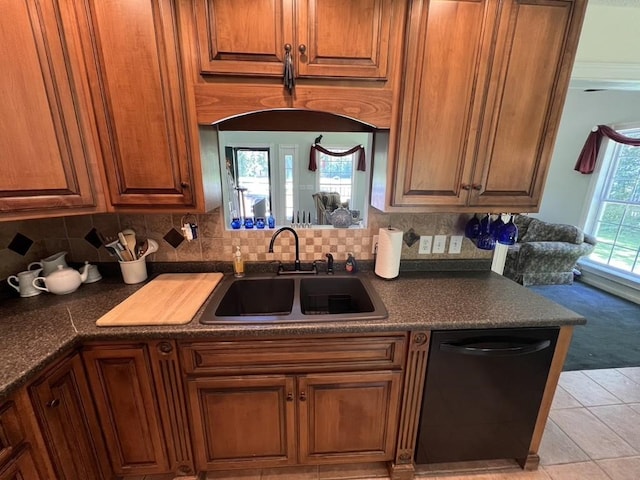 kitchen with backsplash, dark countertops, black dishwasher, a sink, and brown cabinetry