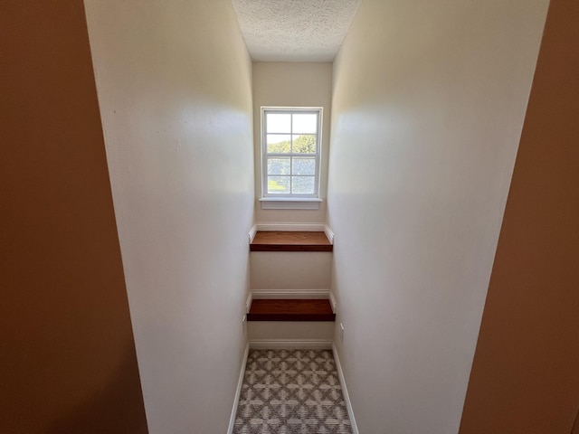 stairway with baseboards, a textured ceiling, and tile patterned floors