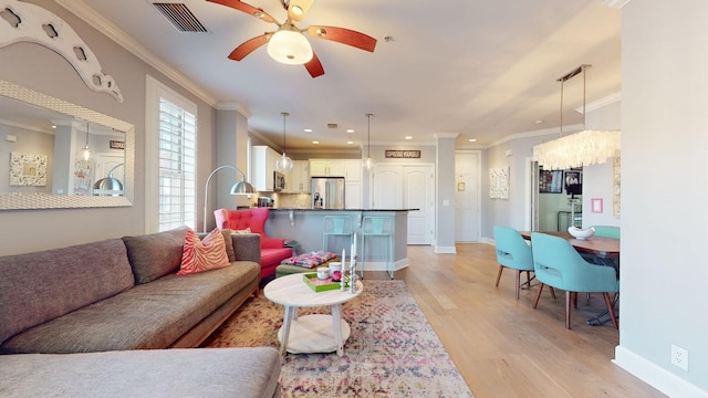 living room with light wood-style flooring, visible vents, a ceiling fan, and ornamental molding