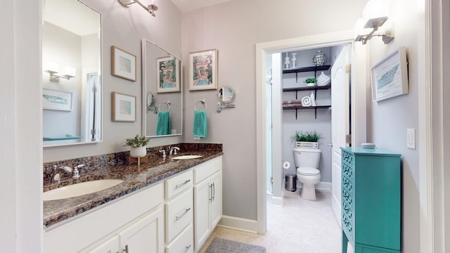 full bath with toilet, a sink, double vanity, and baseboards