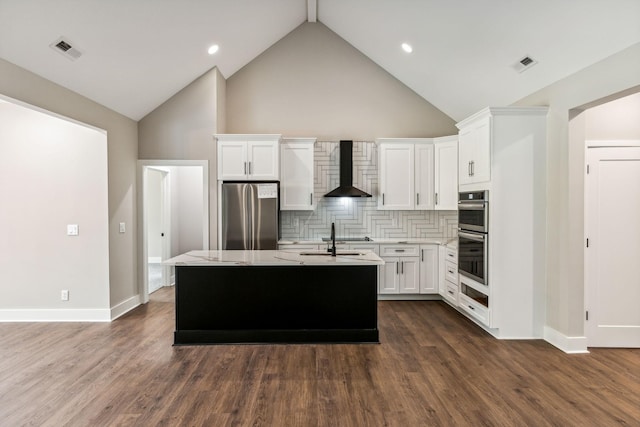 kitchen featuring light countertops, wall chimney exhaust hood, a center island with sink, appliances with stainless steel finishes, and white cabinetry