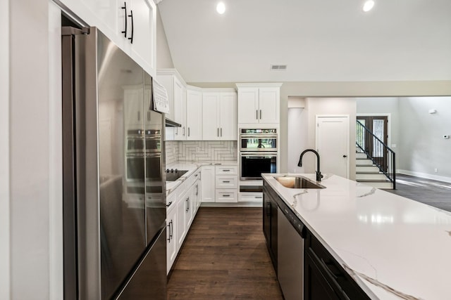 kitchen featuring light stone counters, a sink, appliances with stainless steel finishes, visible vents, and decorative backsplash