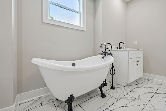 bathroom featuring marble finish floor, baseboards, a soaking tub, and vanity