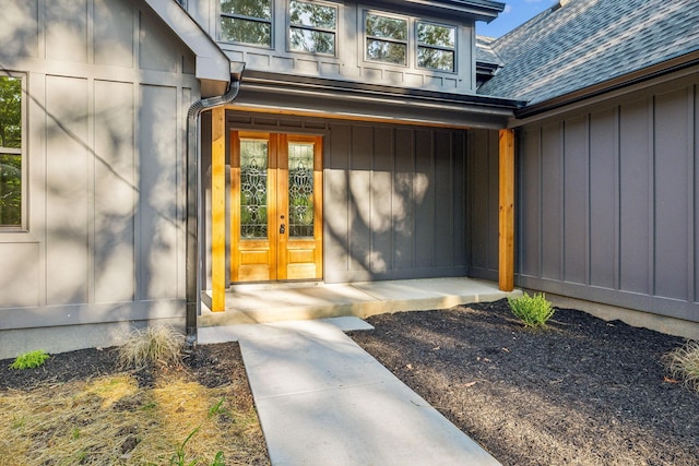 view of exterior entry with board and batten siding, french doors, and roof with shingles